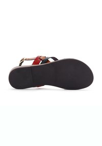 Sandale multicolore avec des lanières tissées noires, des accents rouges et une semelle noire lisse. Détail de boucle ajustable sur la lanière de cheville.