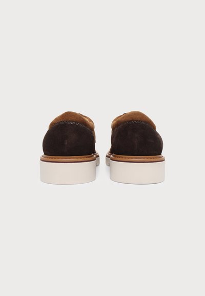 Paire de chaussures en daim marron avec des semelles épaisses blanches, vues de dos sur un fond clair uni.