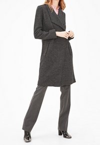 Gray wool coat with a double-breasted design, wide lapels, two front pockets, and a relaxed fit, worn over gray trousers and black heels.