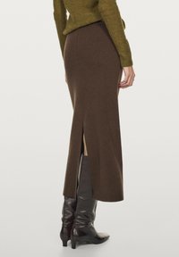 Bruine gebreide midi rok met een rugsplit, gecombineerd met glanzende zwarte knielange laarzen. Zachte textuur en slank design.