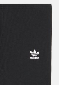 Leggings côtelés noirs avec un logo Trefoil blanc d'Adidas. Dotés d'une taille élastique et d'un design ajusté pour le confort et la flexibilité.