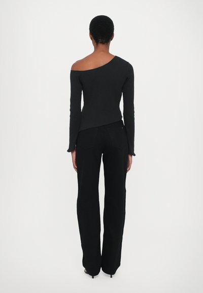 Top nero a spalla unica e manica lunga abbinato a pantaloni neri a gamba larga. Il tessuto appare liscio con un design aderente. Orlo leggermente curvo sul retro.