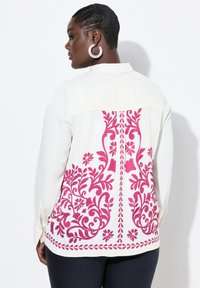 Weiße Bluse mit einem rosa Blumenmuster auf dem Rücken, mit langen Ärmeln und einem knöpfbaren Bündchen, aus einem glatten Stoff gefertigt.