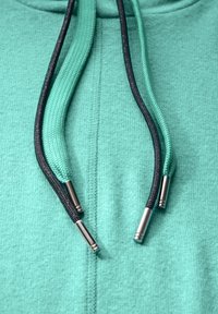 Mintgrüner Kapuzenpulli aus einem strukturierten Stoff; ausgestattet mit zwei kontrastierenden Kordeln – eine mintgrün und eine schwarz – mit metallischen Spitzen.