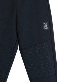 Dunkelblaue Jogginghose mit strukturiertem Paneeldesign und dem Aufdruck "PLAY ALL DAY". Hergestellt aus weichem Stoff mit gerippten Akzenten in der Kniehöhe.