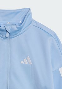Helles blaues Sportjackett mit hohem Kragen, Reißverschluss und silbernem Adidas-Logo. Verfügt über einen glatten, strukturierten Stoff und ein sportliches Design.