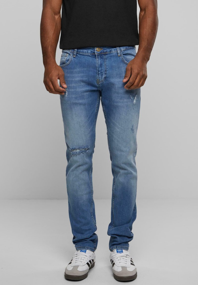 Világoskék, slim fit farmerek, gyűrődéssel, térdnél szakításokkal és klasszikus öt zsebes dizájnnal.