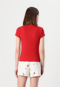 Rød ribbet kortærmet top med en tætsiddende silhuet, parret med cremede shorts med et multicolor blomsterdesign.