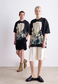 Storede sorte t-shirts med grafiske designs, der viser træer og arkitektur. Sæt dem sammen med sort-hvide shorts, lædersko og cowboystøvler.