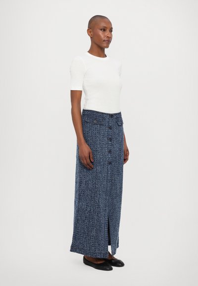 Denim maxi-seelik tekstuuriga sinisest kangast, esi-nöörid ja külgslait. Kombineeritud sobiva valge lühikese varrukaga topiga ja mustade kingadega.