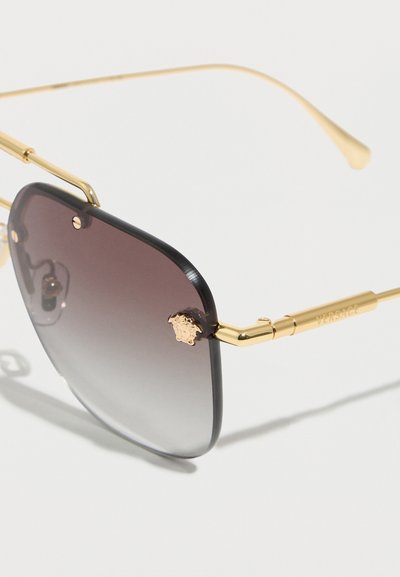 Τετράγωνα φακοί με γκράντιεντ γκρι απόχρωση, με χρυστό μεταλλικό πλαίσιο και βραχίονες, διακοσμημένοι με μικρό χρυσό έμβλημα Μέδουσας στην γωνία του φακού και τη λέξη "Versace" στον βραχίονα.