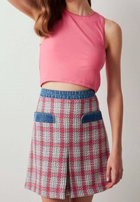 Top corto rosa sin mangas sobre una falda de cuadros con cinturilla y bolsillos de mezclilla. La falda presenta patrones en verde, rosa y blanco en un tejido texturizado.