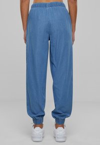 Joggers de denim azul con cintura y puños elásticos, que presentan un ajuste holgado y una textura suave, combinados con zapatillas blancas.