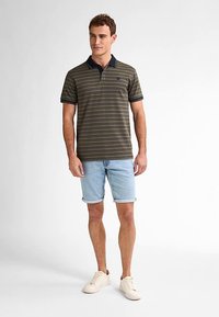 Miesten lyhythihainen oliivinvihreä poolopaita, jossa on tummansinisiä raitoja ja kaulus, yhdistettynä vaaleisiin farkkushortseihin ja kermanvärisiin tennareihin.