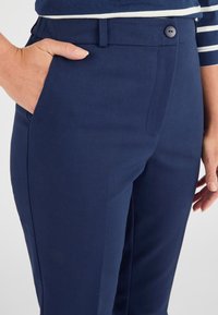 Pantaloni blu navy in tessuto liscio con taglio dritto. Presentano una chiusura con bottone e tasche laterali, con un aspetto elegante e sartoriale.