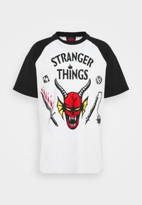 Camiseta de manga corta con cuerpo blanco y mangas raglán negras que presenta un gráfico de calavera roja con cuernos amarillos y varios íconos de armas.