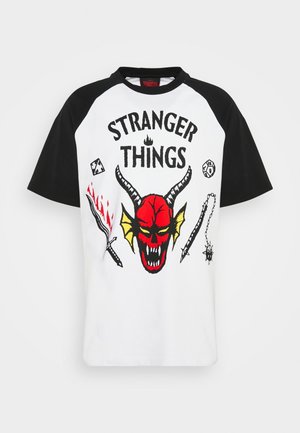 Kurzarm-T-Shirt mit weißem Körper und schwarzen Raglan-Ärmeln, das ein rotes Totenkopf-Design mit gelben Hörnern und verschiedenen Waffensymbolen zeigt.