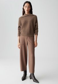 Bruine, getextureerde gebreide trui met een kraag, gecombineerd met hoogwaardige bruine broeken met voorzakken. Zwarte enkelboots maken de outfit compleet.