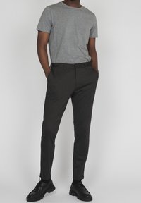 Grå kortärmad t-shirt i kombination med mörka byxor och svarta skor. T-shirten har en jämn textur och byxorna har en klassisk passform med fickor.