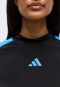 Primo piano di una persona che indossa una maglietta sportiva nera con il logo Adidas blu e strisce sulle spalle visibili.