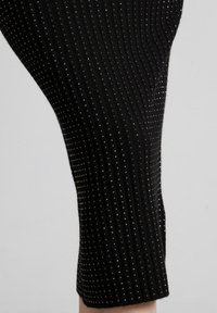 Czarne legginsy prążkowane z wzorem małych metallicznych ćwieków. Materiał ma gładką teksturę i dopasowany krój z subtelnym połyskiem.