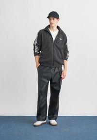 Μαύρο φλις μπουφάν με άσπρες ρίγες, σχέδιο με φερμουάρ; συνδυασμένο με μαύρο, κομψό παντελόνι; άτομο με μαύρο καπέλο και άσπρα αθλητικά παπούτσια.