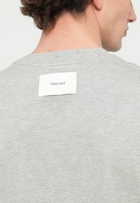 Γκρι κοντομάνικο μπλουζάκι με στρογγυλή λαιμόκοψη, με υφή και ορθογώνια ετικέτα με τη λέξη "Selected" στην πίσω πλευρά του λαιμού.