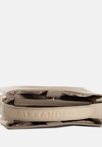 Borsa a mano in pelle beige con esterno texturizzato, hardware dorato e logo impresso sulla tracolla. L'interno presenta una tasca con zip.