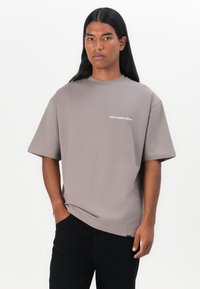 Camiseta gris de gran tamaño con mangas cortas y cuello redondo, que presenta el texto blanco "no desperdicies la cultura" en el área del lado izquierdo del pecho.