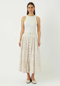 Hvitt ribbet tanktopp kombinert med et langt, mønstrete skjørt med et beige og elfenbensfarget blomstermønster, knappestenging og plisserte detaljer.