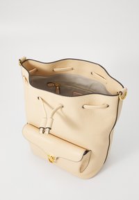 Beige läder bucket-väska med texturerad yta, snörning som stängning och en framficka säkrad med ett spänne i guldton. Inuti foder i tyg.