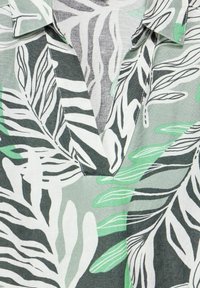 Collared shirt in light green, white, and black featuring a leaf pattern; soft fabric with a V-neckline and visible stitching details.