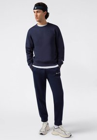 Sudadera de algodón en color azul marino con cuello redondo y logotipo bordado, combinada con pantalones jogger a juego. Cuenta con puños y cintura de canalé.