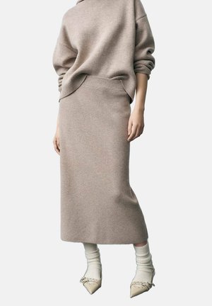 Beige gebreide trui met een losse pasvorm en verlaagde schouders, gecombineerd met een bijpassende strakke rok en crèmekleurige kniekousen.