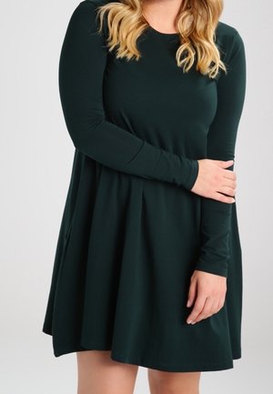 Donkergroene lange mouwen jurk van zachte stof. Heeft een getailleerde bovenkant en een uitlopende rok met een gladde textuur en een minimalistisch ontwerp.