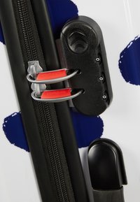 Bagages noir et blanc avec des pois bleus, présentant une fermeture éclair noire et des accessoires en métal rouge, ainsi qu'une surface texturée.