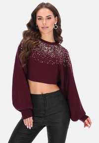 Bordeaux cropped sweater met versierde halslijn, lange volumineuze mouwen en textuurstof; gecombineerd met zwarte getailleerde broek.