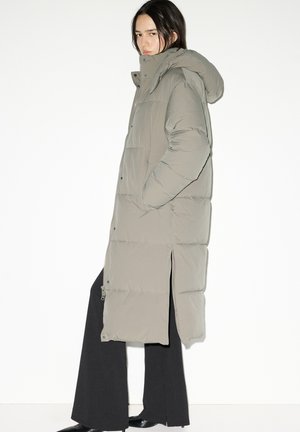 Duga, svijetlosiva puhasta jakna s kapuljačom, zatvaranjem na patentni zatvarač i bočnim prorezima za lakše kretanje. Nošena preko crnih hlača i čizama.