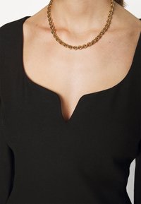 Gros plan d'une personne portant une chaîne en or et un haut noir avec un décolleté profond en forme d'encoche.