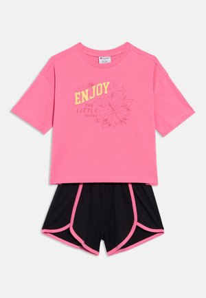 Camiseta rosa de manga corta con la frase "DISFRUTA DE LAS PEQUEÑAS COSAS" en amarillo, combinada con pantalones cortos negros con ribete rosa y diseño de ajuste holgado.