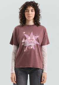 Bordowy t-shirt z krótkim rękawem, ozdobiony wzorem gwiazdy oraz napisem "AFTER MIDNIGHT" z błyszczącymi dodatkami. Nałożony na wzorzystą koszulę z długim rękawem.
