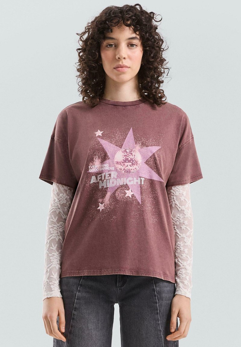 Bordowy t-shirt z krótkim rękawem, ozdobiony wzorem gwiazdy oraz napisem "AFTER MIDNIGHT" z błyszczącymi dodatkami. Nałożony na wzorzystą koszulę z długim rękawem.