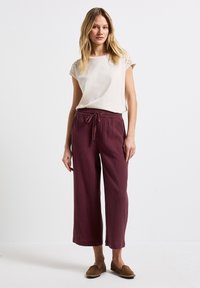 Beige top met kant op de schouders, gecombineerd met losse, bordeauxkleurige, gestructureerde broek met elastische tailleband en trekkoord. Bruine instappers.