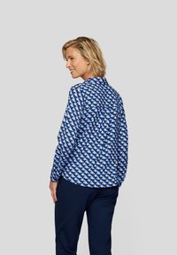 Langarmhemd mit einem blauen geometrischen Muster, mit Knopfkraagen und einer lockeren Passform, kombiniert mit marinefarbenen Hosen.