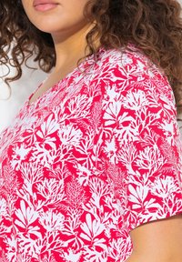 Tričko s krátkým rukávem, které se vyznačuje živým červenobílým korálovým vzorem, má výstřih do V a je vyrobeno z měkké, lehké tkaniny.