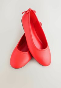 Raudonos odinės baleto bateliai su glotniu paviršiumi, apvalia nosimi ir dekoratyvine kaspinu kulne. Minimalistinis dizainas su lygia pado dalimi.