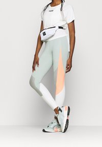 Leggings gris claro con un acento coral, combinados con una camiseta blanca y una riñonera blanca. Completado con zapatillas azul claro.