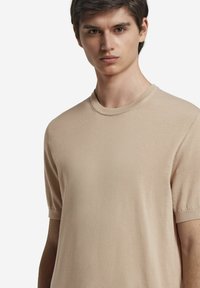 Beige kortærmet sweater med rund halsudskæring, lavet af et blødt, let stof. Har en glat overflade og tætsiddende ærmer.