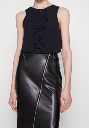 Blouse noire sans manches avec détail volanté sur le devant, associée à une jupe en cuir noire taille haute avec une fermeture éclair diagonale argentée.
