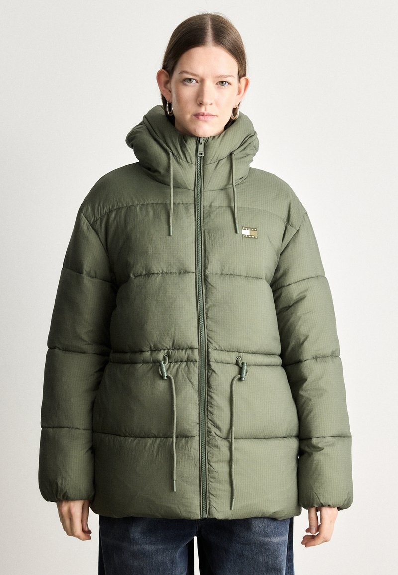 Giacca puffer verde con colletto alto, coulisse regolabili e cuciture orizzontali. Presenta un piccolo logo sul petto e una chiusura con zip.